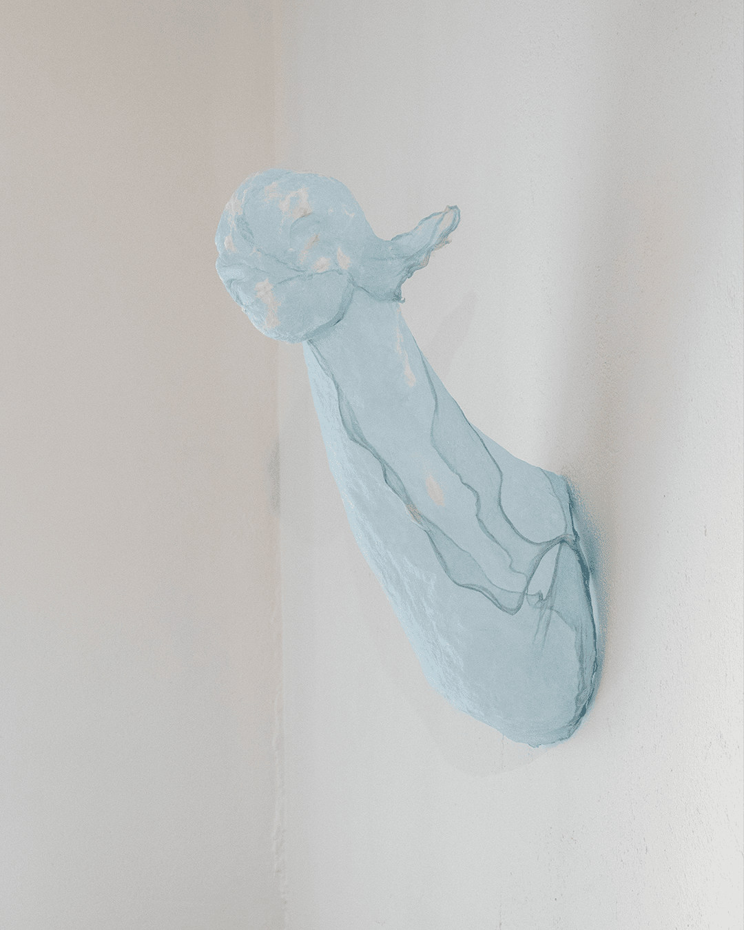 A pale blue, translucent, organic sculpture is mounted on a plain white wall, extending outward from the corner.