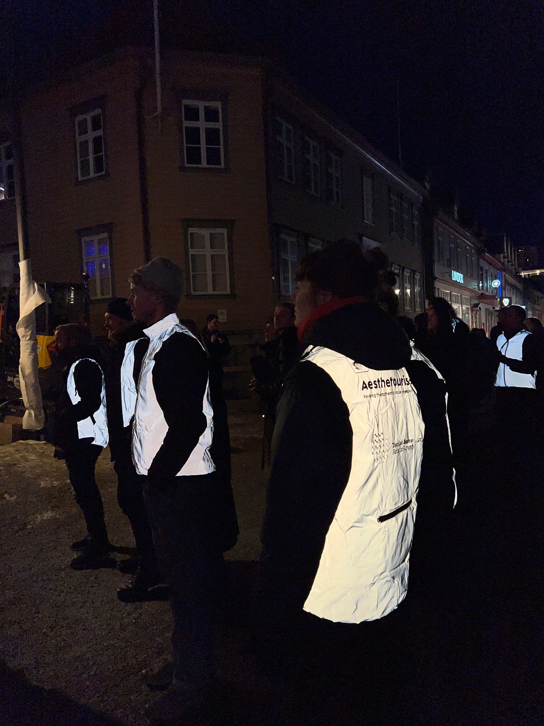 People wearing reflective vests with "Aesthetourist" branding stand on a dark city street at night in front of old buildings.